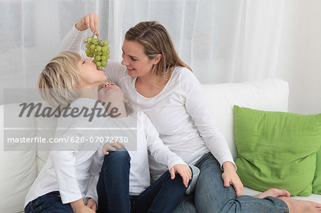 Mother and two children eating grapes on couch