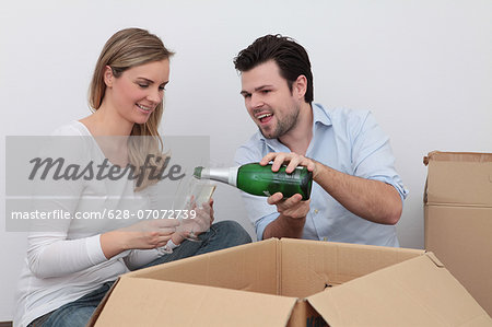 Couple celebrating with champagne amidst moving boxes