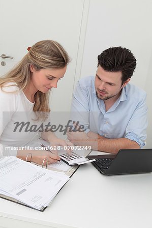Man and woman sitting at table with file, calculator and laptop