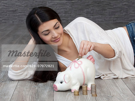 Young woman putting coin into piggy bank