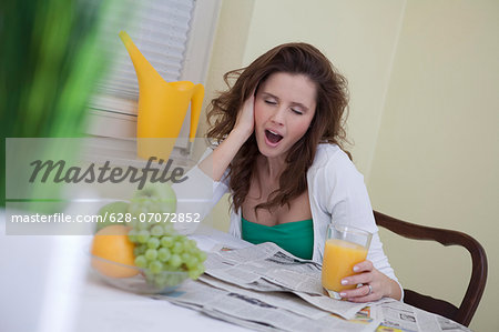 Young woman yawning at breakfast table