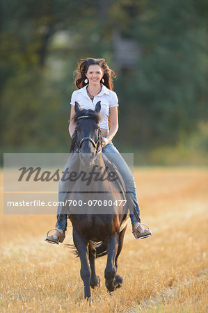 Portrait of young woman riding a Friesian horse in a cut cornfield, Bavaria, Germany