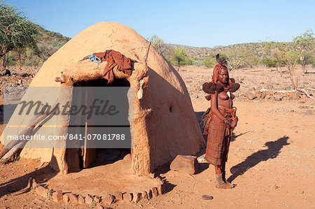 Young Himba woman standing outside her traditional mud-covered dwelling in a Himba village in the Kunene Region (formerly Kaokoland) in the far north of Namibia