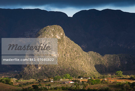 View across Vinales Valley, UNESCO World Heritage Site, from Hotel Los Jasmines in stormy weather showing one of the limestone Magotes lit by the sun against mountains in shade, Vinales, Pinar Del Rio Province, Cuba, West Indies, Central America