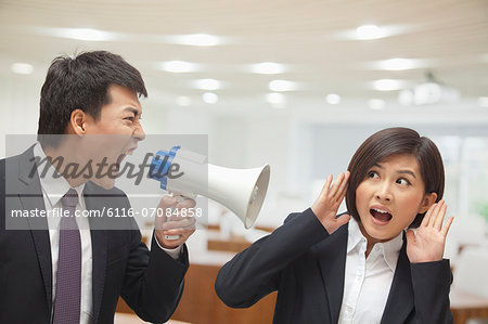 Businessman Talking into Megaphone by Businesswoman's Ear