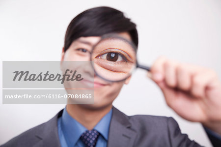 Young businessman looking through magnifying glass, studio shot