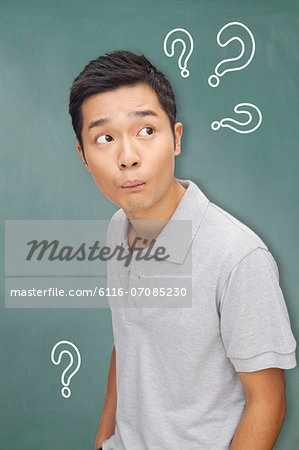 Portrait young man in front of blackboard with question marks