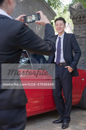 Businesswoman Taking Businessman's Picture Next to His Car