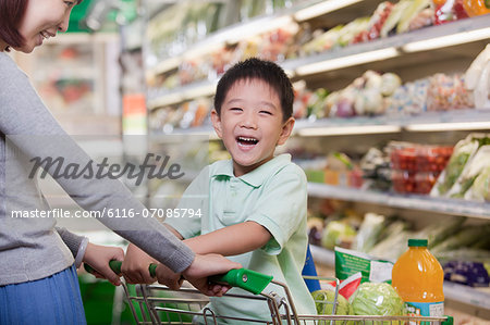 Young boy smiling, sitting in a shopping cart, shopping with mother