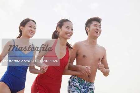 Three friends holding hands and smiling on the beach