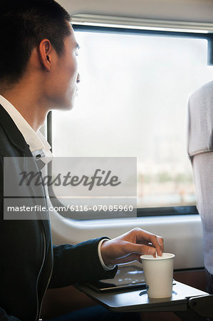 Man Looking Through Train Window While Stirring His Coffee
