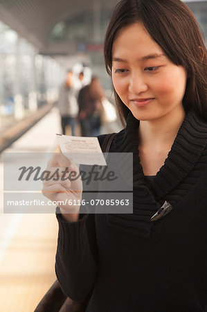 Young Woman Looking At Train Ticket on Railroad Platform