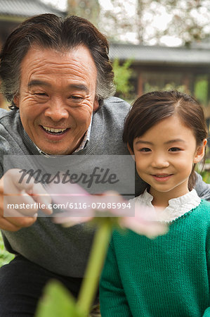 Grandfather and granddaughter looking at flower in garden