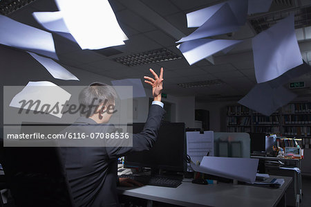 White-collar worker throwing white sheets in air in office