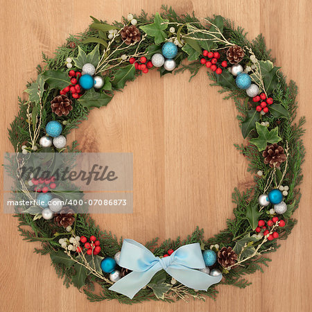 Christmas floral wreath decoration with blue and silver baubles, bow, holly and winter greenery over oak background.