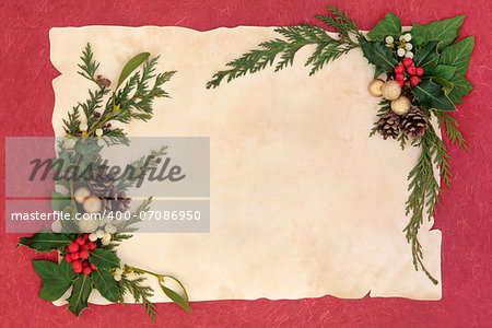 Christmas and winter floral border with gold baubles, natural holly, mistletoe, ivy, fir leaf sprigs and pinecones over old parchment and red background.