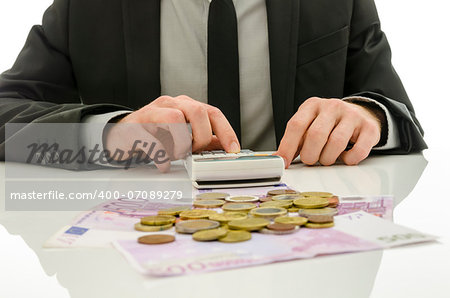 Detail of businessman working on calculator counting expenses. With Euro coins and banknotes on his white table.