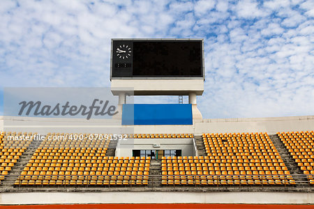 Rows of orange seats on the stadium with scoreboard displaying clock above them