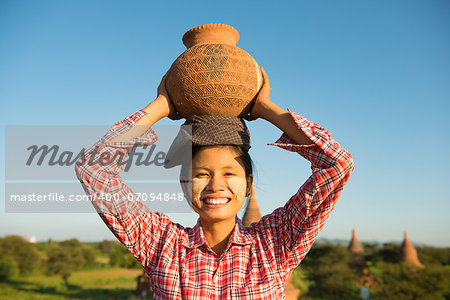 Portrait of Asian traditional female farmer carrying clay pot on head going back home, Bagan, Myanmar