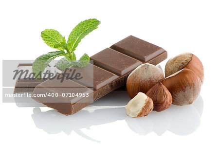Closeup detail of chocolate parts, hazelnuts and mint leaves on white background.