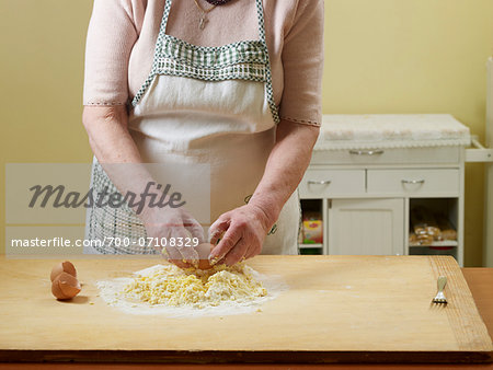 Elderly Italian woman making dough by hand in kitchen, cracking eggs into flour, Ontario, Canada
