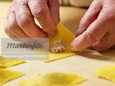 Close-up of elderly Italian woman's hands making ravioli pasta in kitchen, adding filling, Ontario, Canada