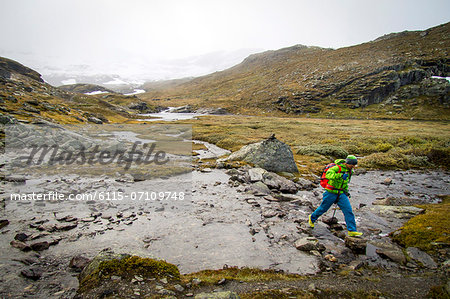 Hiker crossing mountain stream, Norway, Europe