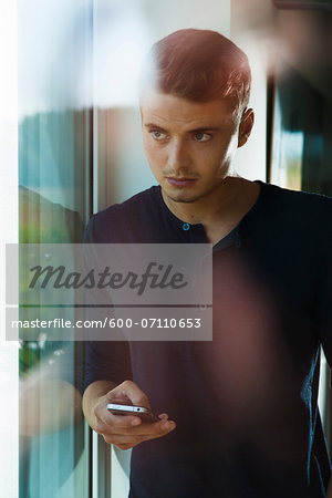 Young Man with Cell Phone Looking out Window, Mannehim, Baden-Wurttemberg, Germany