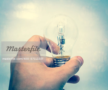 A hand holding a lightbulb against blue background