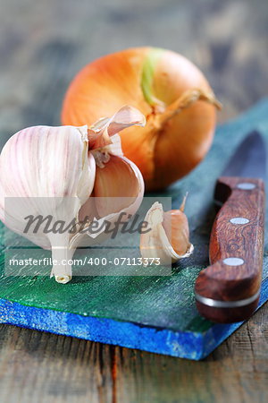 Garlic, onions and knife on blue board.