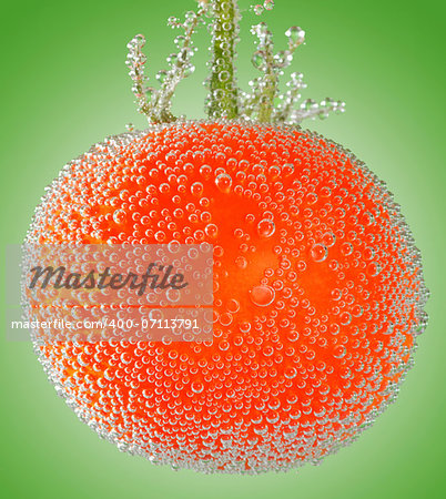 A fresh organic tomato immersed in mineral water on green background