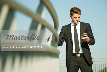 Portrait of businessman standing by railing and looking at smartphone, Germany Portrait of businessman standing by railing and looking at smartphone, Germany