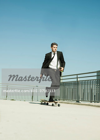 Businessman skateboarding on walkway holding binder, Germany Businessman skateboarding on walkway holding binder, Germany