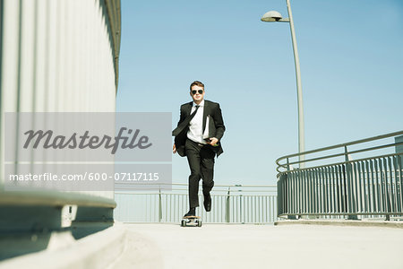 Businessman skateboarding on walkway holding binder, Germany Businessman skateboarding on walkway holding binder, Germany