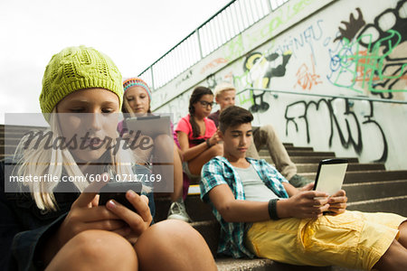 Group of children sitting on stairs outdoors, using tablet computers and smartphones, Germany