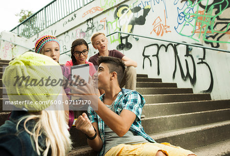 Group of children sitting on stairs outdoors, using tablet computers and smartphones, Germany Group of children sitting on stairs outdoors, using tablet computers and smartphones, Germany