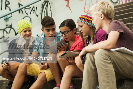 Group of children sitting on stairs outdoors, using tablet computers and smartphones, Germany