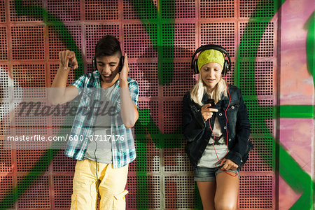 Children standing next to wall outdoors, wearing headphones and listening to music, Germany