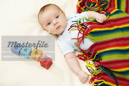 Baby boy lying under striped blanket with blocks spelling baby