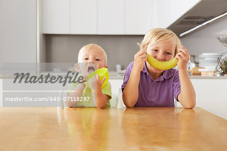 Brothers playing with bowl and banana at table