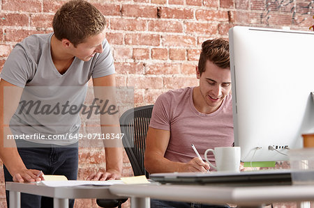 Young men talking at desk with computer