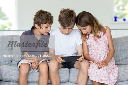 Brothers and sister on sofa looking at digital tablet