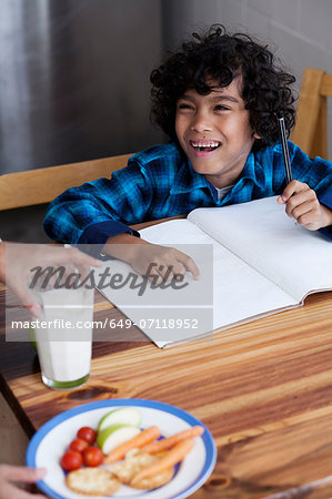 Boy doing homework, person serving snacks and milk