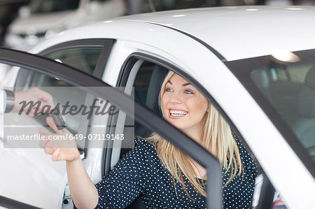 Young woman sitting in new car with key in showroom