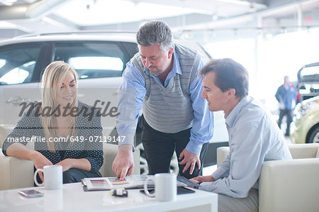 Car salesman advising couple in car showroom