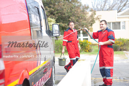 Paramedics cleaning ambulance with hosepipe