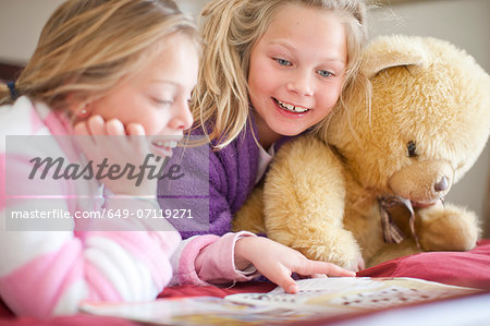 Sisters and teddy bear reading storybook