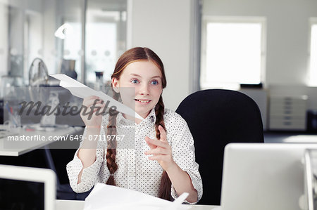 Girl holding paper airplane in office
