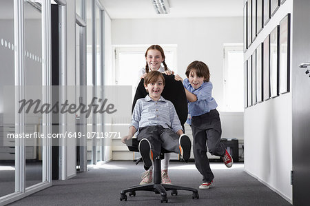 Three children playing in office corridor on office chair