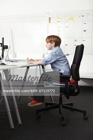 Boy sitting on ring binders on office chair using computer Boy sitting on ring binders on office chair using computer